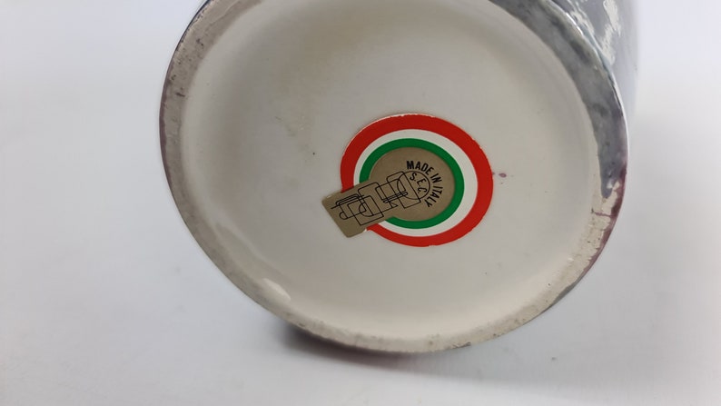 Puede incluir: Un jarr&oacute;n de cer&aacute;mica con interior blanco y exterior oscuro. La base presenta una pegatina con el texto "MADE IN ITALY" en un dise&ntilde;o circular con colores rojo, blanco y verde.