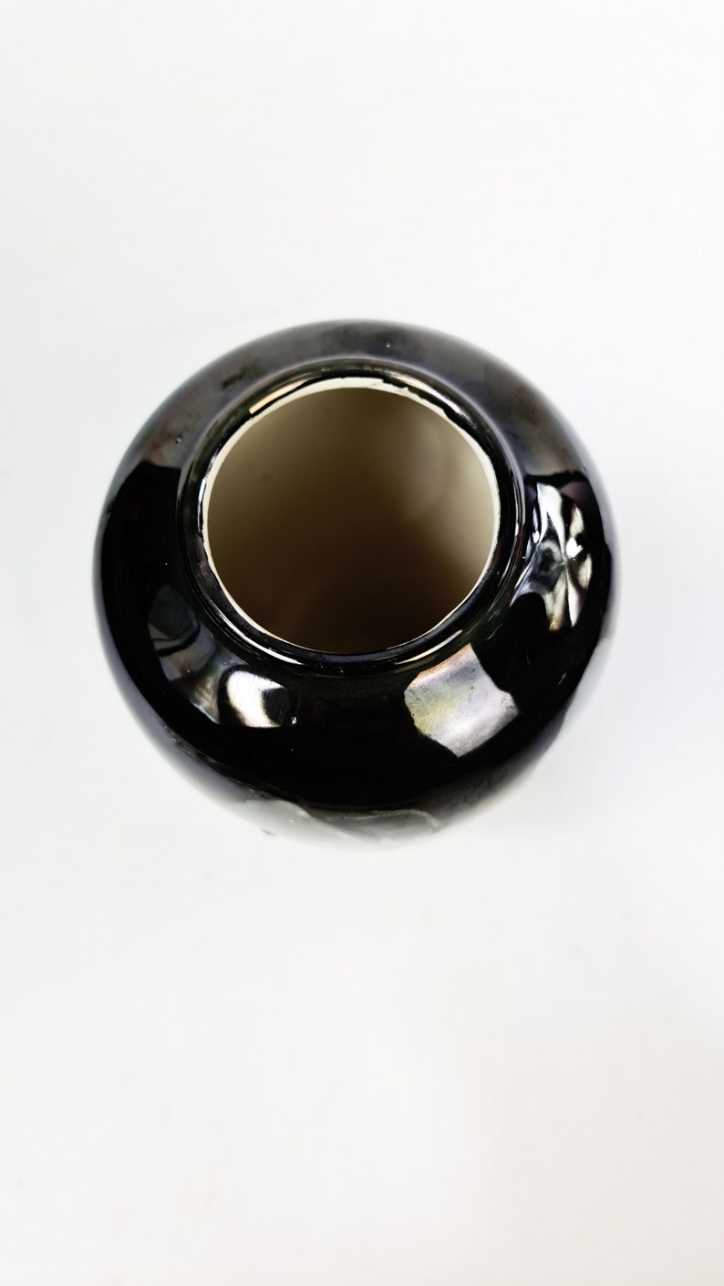 Puede incluir: Un jarr&oacute;n de cer&aacute;mica negro brillante con cuerpo redondo y boca ancha. El interior es de color marr&oacute;n claro, contrastando con el exterior. El jarr&oacute;n est&aacute; sobre un fondo blanco.