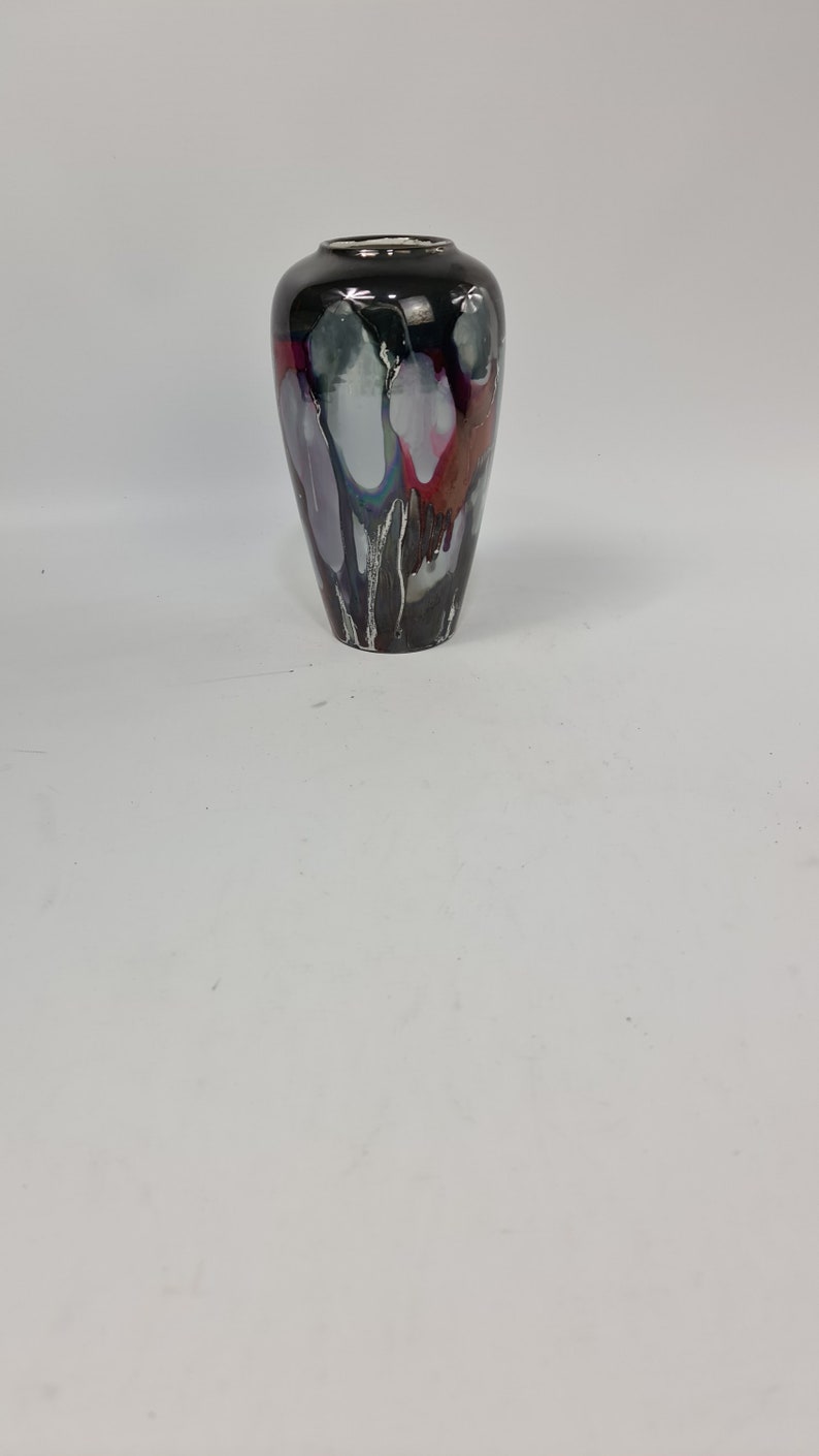 Puede incluir: Un jarr&oacute;n decorativo con un acabado negro brillante y un dise&ntilde;o abstracto &uacute;nico. El jarr&oacute;n presenta vetas blancas, grises, moradas y rojas, creando un efecto visual llamativo. Tiene un cuello estrecho y un cuerpo m&aacute;s ancho, ideal para arreglos florales.