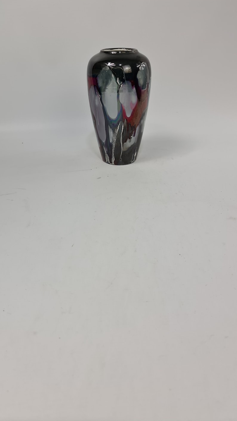 Puede incluir: Un jarr&oacute;n decorativo alto con acabado negro brillante. El jarr&oacute;n presenta un dise&ntilde;o &uacute;nico con vetas blancas, grises, rojas y moradas. Tiene un cuello estrecho y un cuerpo m&aacute;s ancho, ideal para flores o como pieza decorativa.