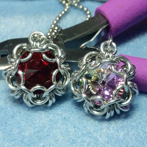 May include: Two silver chainmaille pendants with red and pink crystal stones in the centre. The pendants are hanging from a silver chain.