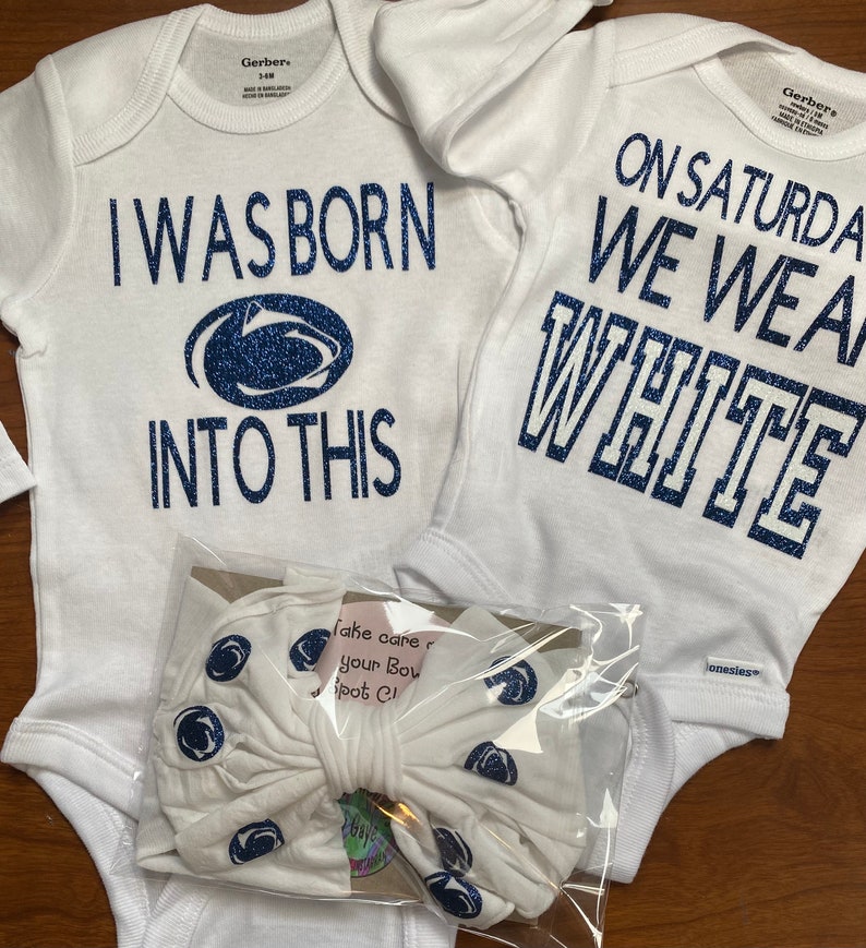 May include: Two white baby onesies with blue glitter text. One onesie says "I was born into this" with a blue glitter Penn State Nittany Lion logo. The other onesie says "On Saturday we wear white". A white headband with blue glitter Penn State Nittany Lion logos is included.