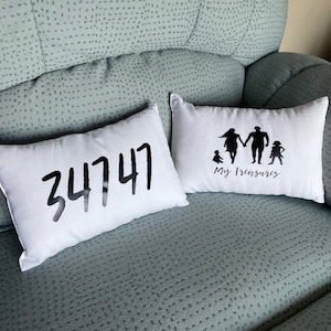 May include: Two white throw pillows with black text and images. One pillow has the number 34747 printed on it. The other pillow has a silhouette of a family with the text "My Treasures" printed below.