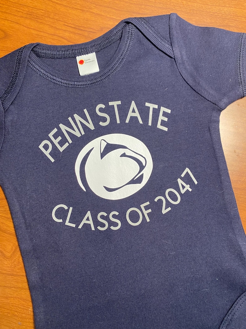 May include: A navy blue baby onesie with a white graphic of the Penn State Nittany Lion mascot and the text "Penn State Class of 2047".