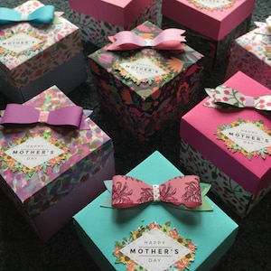 May include: Six small square gift boxes with floral patterns and pink, blue, and green colors. Each box has a bow and a label that says "Happy Mother's Day".