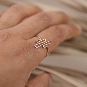Puede incluir: Un anillo de oro con un diseño abstracto simple. El anillo se lleva en un dedo.