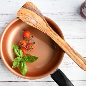 Peut inclure: Une poêle de cuisson en cuivre avec une poignée noire, une cuillère en bois et une branche de basilic avec des tomates cerises rouges.