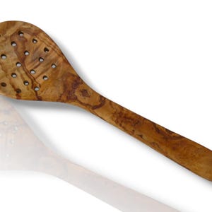 May include: A wooden slotted spoon with a long handle and a round head. The spoon is made of olive wood, featuring a natural wood grain pattern. The head has multiple holes for draining liquids.