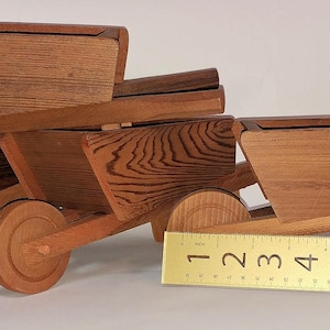 May include: Three wooden toy wheelbarrows stacked on top of each other. The wheelbarrows are made of different types of wood and have a natural finish. The wheelbarrows are all different sizes, with the smallest on top and the largest on the bottom.