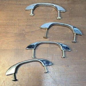 May include: Four silver-toned metal drawer pulls with a curved, arching design. Each handle features two attached threaded mounting screws extending downward, providing a secure attachment point for installation on cabinets or furniture drawers.