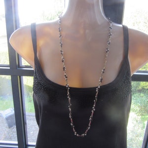 Peut inclure: Un long collier en chaîne argentée avec des perles noires et blanches. Le collier est porté par un mannequin vêtu d'un débardeur noir.
