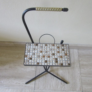 May include: A black metal side table with a tiled top. The table has a single shelf and a curved metal arm. The tile is a mosaic of white, brown, and beige squares.