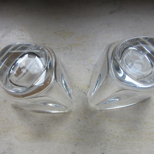 May include: Two clear glass candle holders with a unique, faceted design. The holders are empty and have a reflective surface.