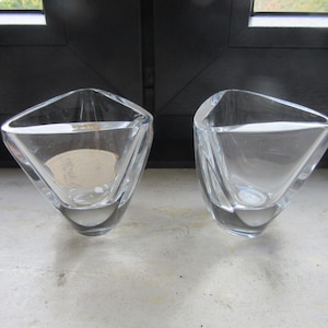 May include: Two clear glass triangular vases with a geometric design. The vases are empty and sitting on a light grey surface.