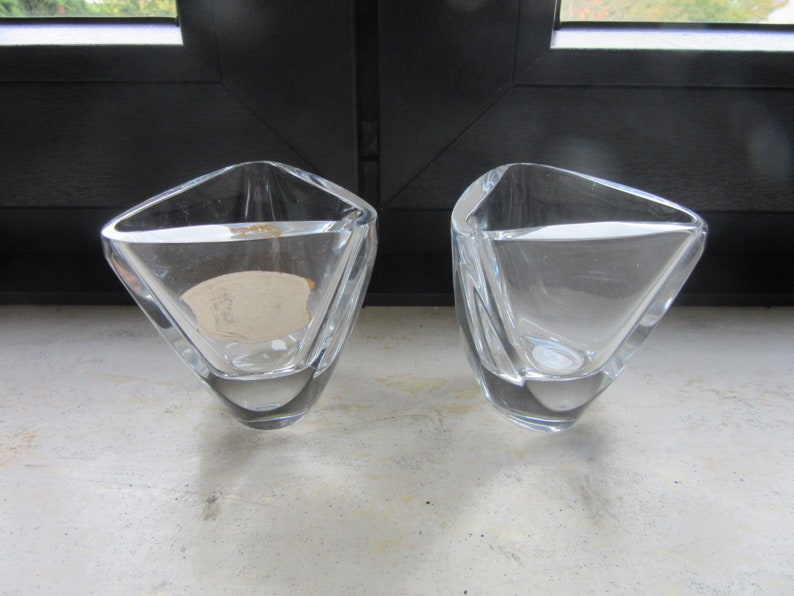 May include: Two clear glass triangular vases with a geometric design. The vases are empty and sitting on a light grey surface.