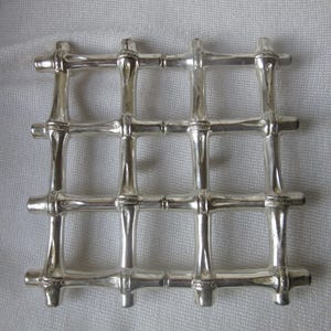 Può includere: Un oggetto argentato a forma di griglia con un design in stile bambù. L'oggetto è composto da più barre orizzontali e verticali che si intersecano per formare una serie di quadrati. Le barre hanno un aspetto strutturato.