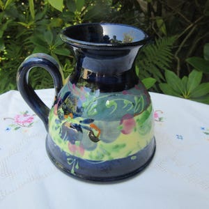 May include: A blue ceramic pitcher with a handle, decorated with a floral design in shades of pink, green, and yellow.