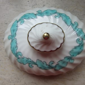 May include: White ceramic lid with a gold trim and a green leafy design. The lid has a small knob on top.