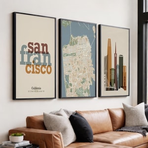 Könnte beinhalten: Drei gerahmte Kunstdrucke mit San Francisco. Der erste Druck zeigt den Stadtnamen in überlagertem Text, der zweite eine Karte und der dritte eine Skyline. Die Drucke befinden sich in schwarzen Rahmen und hängen über einem braunen Ledersofa.