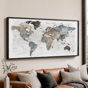 May include: A rectangular wall art piece featuring a world map in a black frame. The map displays continents and oceans in a muted colour palette of charcoal, slate grey, and soft beige tones, with printed text identifying major countries and regions.