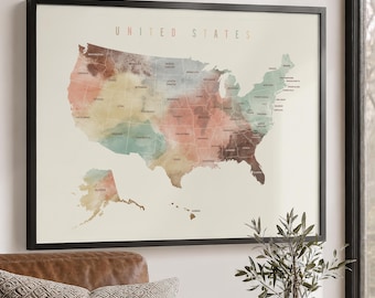 May include: A framed wall art print featuring a map of the United States with a watercolor aesthetic. The map displays state boundaries and names in a muted color palette of soft greens, browns, and tans against a light cream background.