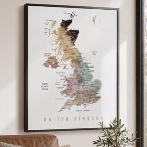 May include: A framed wall map of the United Kingdom featuring a gradient color scheme that transitions from dark brown in the north to light green and tan in the south. The map includes labels for major cities, regions, and surrounding bodies of water.