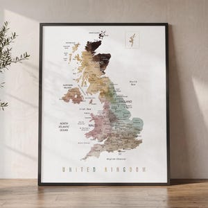 May include: A framed wall art print featuring a detailed map of the United Kingdom. The map displays geographical regions in muted, earthy tones including brown, tan, and sage green. The text UNITED KINGDOM is printed in a clean font at the bottom.