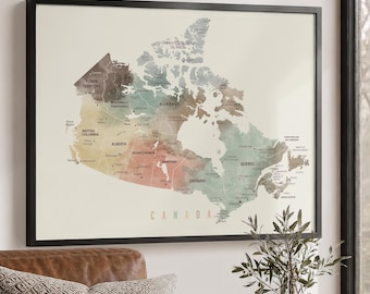 May include: A framed wall map of Canada featuring a watercolor aesthetic with muted earth tones. The map displays provinces, territories, and major cities with clear text labels. The word CANADA is printed in a simple sans-serif font at the bottom.