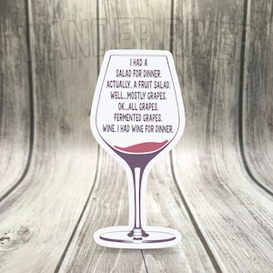 Könnte beinhalten: Ein weißes Weinglas mit einer roten Weinfülllinie und einem humorvollen Textüberlagerung, der lautet: "Ich hatte einen Salat zum Abendessen. Eigentlich einen Obstsalat. Naja...meistens Trauben. Ok...nur Trauben. Fermentierte Trauben. Wein. Ich hatte Wein zum Abendessen."