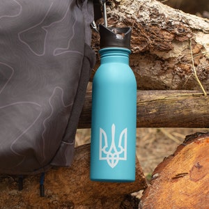 May include: A light blue water bottle with a black lid and a white Ukrainian trident symbol. The bottle is sitting on a wooden log.
