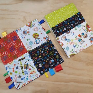 Puede incluir: Una manta sensorial para bebés multicolor con diferentes texturas y patrones. La manta está hecha de tela suave y tiene una variedad de colores, incluyendo rojo, azul, verde, amarillo y negro. La manta presenta una variedad de patrones, incluyendo números, letras y animales. La manta tiene varias cintas atadas a ella, que se pueden usar para el juego sensorial.