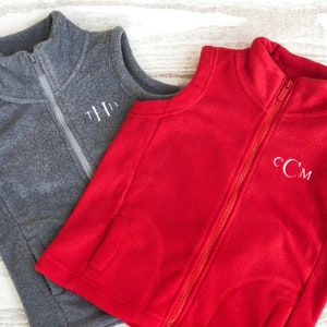 May include: Two fleece vests, one grey and one red, with white embroidered initials. The grey vest has the initials "THD" and the red vest has the initials "CCM".