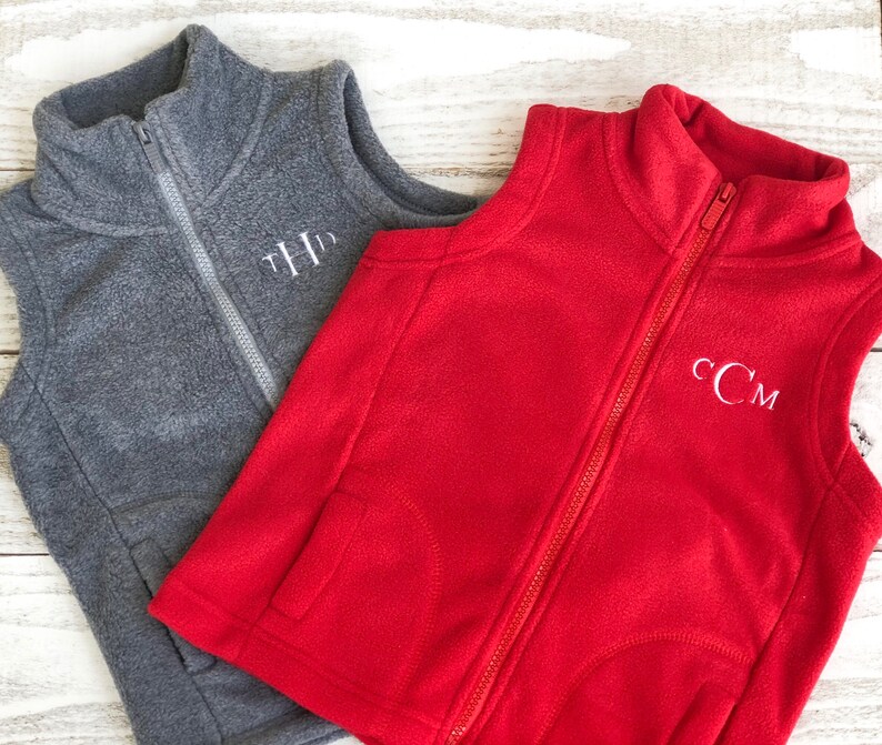 May include: Two fleece vests, one grey and one red, with white embroidered initials. The grey vest has the initials "THD" and the red vest has the initials "CCM".