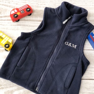 May include: A navy blue fleece vest with a zip fastening and two pockets. The vest has the name "GAM" embroidered on the front.