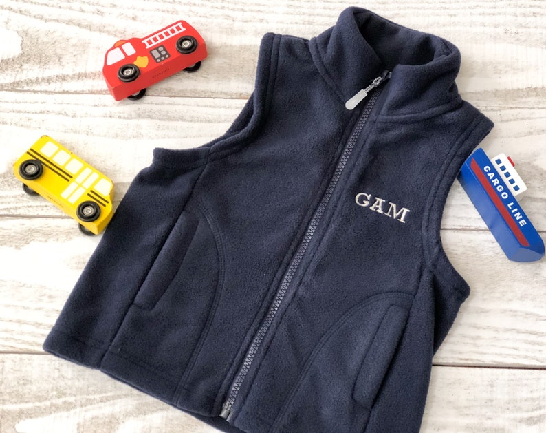 May include: A navy blue fleece vest with a zip fastening and two pockets. The vest has the name "GAM" embroidered on the front.