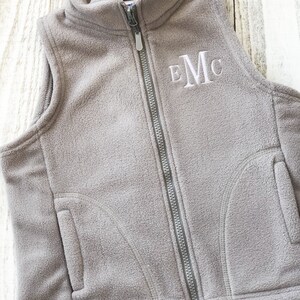 May include: A grey fleece vest with a zip fastening and a white embroidered monogram "EMC".