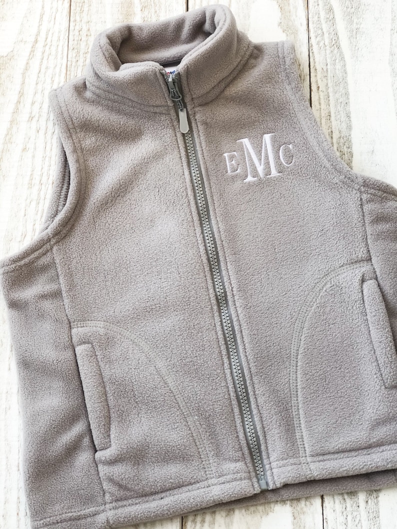 May include: A grey fleece vest with a zip fastening and a white embroidered monogram "EMC".
