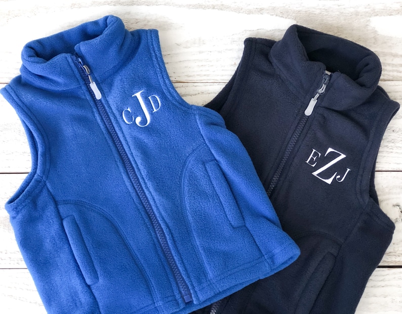 May include: Two fleece vests with zip fastenings. The vest on the left is blue with white embroidered initials "CJD". The vest on the right is navy blue with white embroidered initials "EZJ".