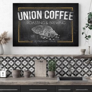 May include: Black and white chalkboard sign with gold trim that reads "Union Coffee, Roasting & Brewing, Established 1988". A white drawing of a bag of coffee beans is in the center of the sign.