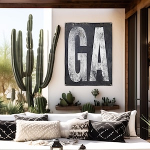 May include: A white couch with black and white patterned pillows in a patio setting. A black and white sign with the letters "GA" is hanging on the wall behind the couch.