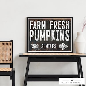 May include: A black framed sign with white text that reads "Farm Fresh Pumpkins 3 Miles" with a rusty metal background and arrows pointing left and right.