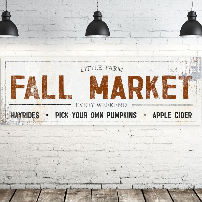 May include: White sign with brown text that reads "Fall Market" with the words "Little Farm" above and "Every Weekend" below. The sign also says "Hayrides, Pick Your Own Pumpkins, Apple Cider".