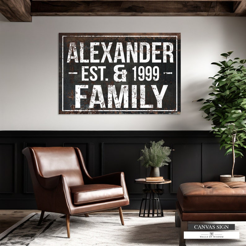 Puede incluir: Un letrero de metal r&uacute;stico con el texto "Alexander Est. & 1999 Family" en letras blancas sobre un fondo oscuro. El letrero est&aacute; colgado en una pared negra con un sill&oacute;n de cuero marr&oacute;n y una mesa peque&ntilde;a delante.
