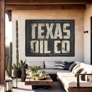 May include: A black and white vintage sign with the text "TEXAS OIL CO" in white lettering. The sign is hanging on a wall in a patio setting with a couch and plants.