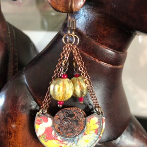 May include: A pair of dangle earrings with a copper chain, two yellow and green beads, and a red and gold patterned crescent moon charm.