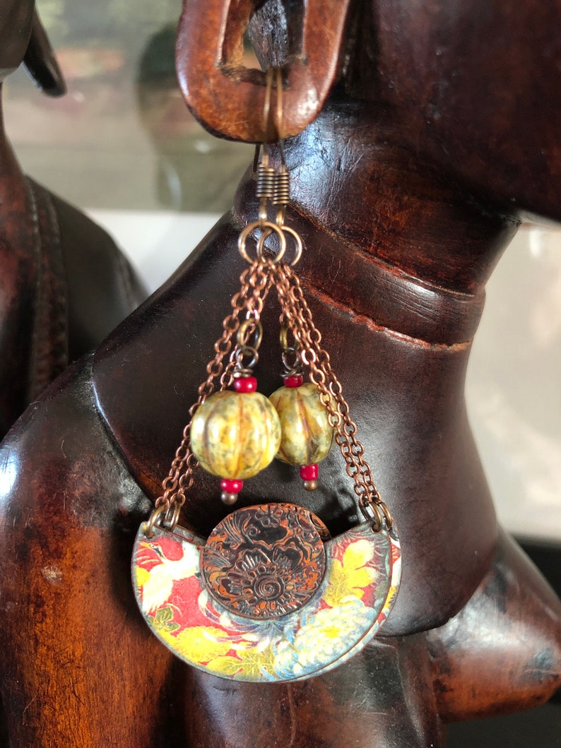 May include: A pair of dangle earrings with a copper chain, two yellow and green beads, and a red and gold patterned crescent moon charm.