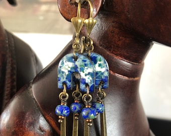 May include: Blue and white ceramic dangle earrings with brass accents and blue glass beads. The earrings have a geometric shape and are suspended from a brass hook.