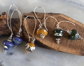 Pendientes bohemios y urbanos, con cuentas de vidrio hilado hechas a mano, cuentas y ganchos de metal bañados en plata, en tonos morados, mostaza y oliva.