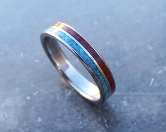 May include: A silver-toned metal ring featuring two distinct inlay channels. One channel contains a textured, bright turquoise blue material, while the adjacent channel is filled with a smooth, deep reddish-brown wood-like material.