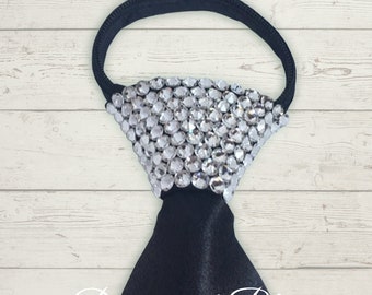 May include: A black satin tie with a large crystal embellishment. The crystals are clear and cover the entire knot of the tie. The tie is on a white wood background.